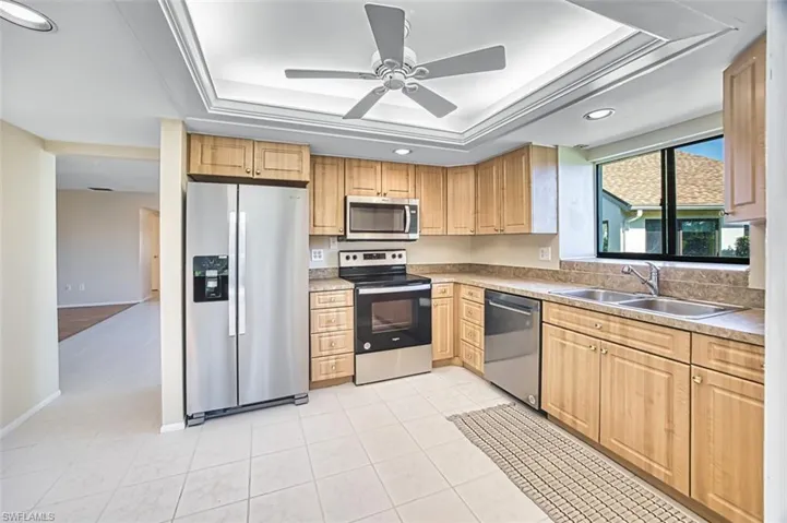Kitchen with stainless steel appliances, a tray ceiling, ceiling fan, light countertops, and recessed lighting