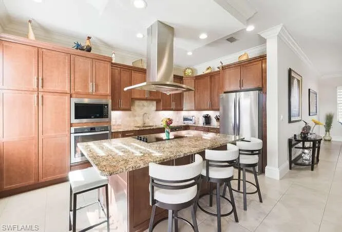 Kitchen with a breakfast bar area, decorative backsplash, crown molding, light stone countertops, and a kitchen island