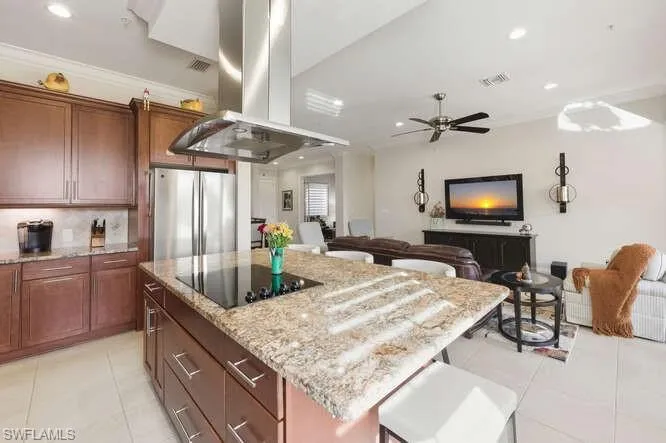 Kitchen featuring open floor plan, island range hood, light stone countertops, a center island, and recessed lighting
