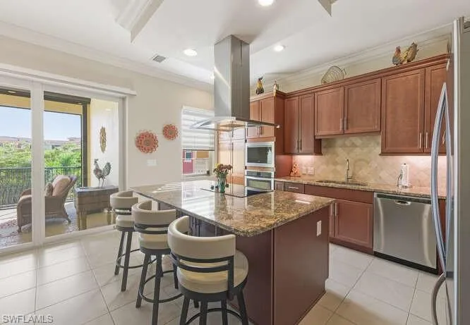 Kitchen featuring ornamental molding, dark stone countertops, decorative backsplash, a breakfast bar area, and a kitchen island