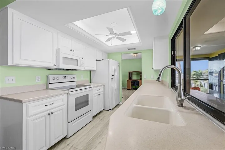 Kitchen with white appliances, visible vents, a sink, white cabinets, and a raised ceiling