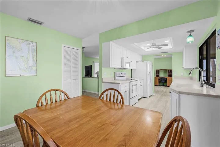 Dining area with baseboards, visible vents, ceiling fan, a raised ceiling, and light wood-type flooring