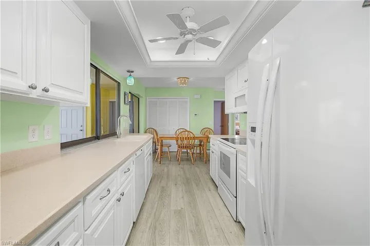 Kitchen with light wood finished floors, white appliances, white cabinetry, and a raised ceiling