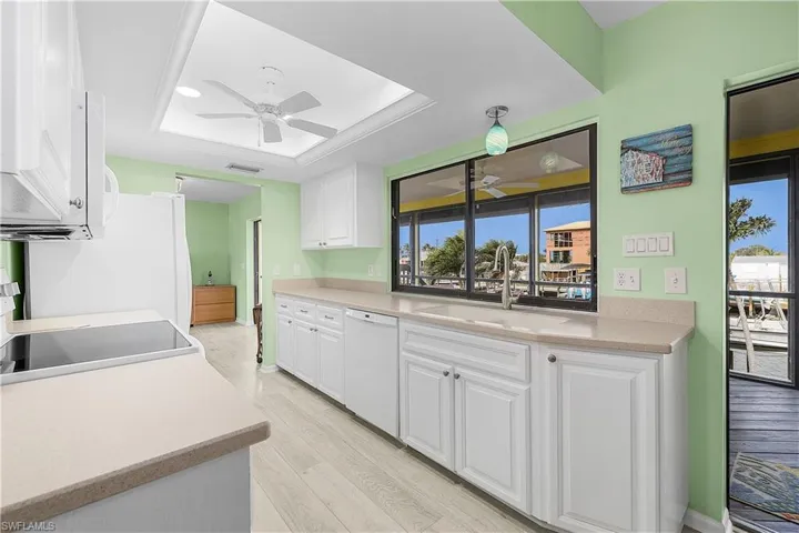 Kitchen with a sink, white appliances, a raised ceiling, and ceiling fan