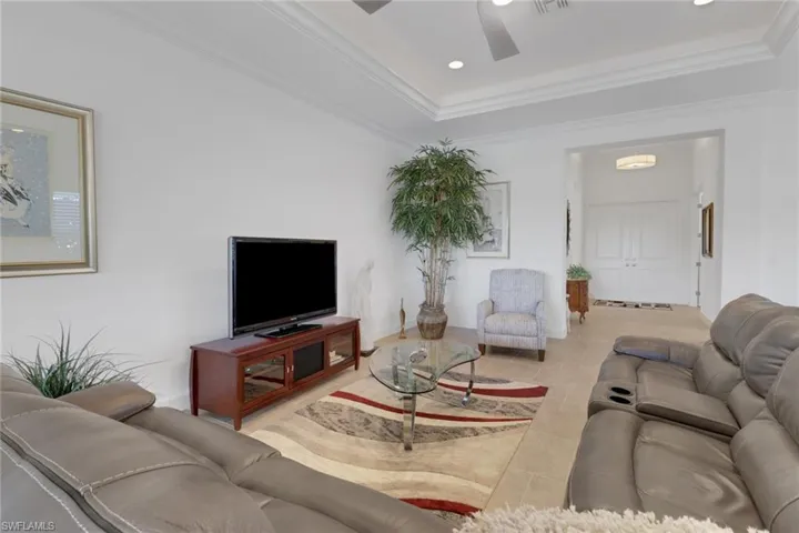 Tiled living room with crown molding, a raised ceiling, and ceiling fan