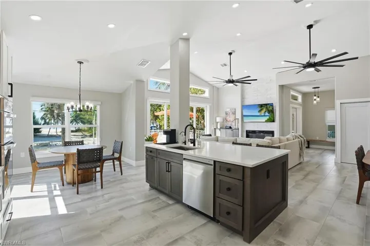 Kitchen featuring a chandelier, stainless steel appliances, vaulted ceiling, a fireplace, and open floor plan - Virtually Edited Image