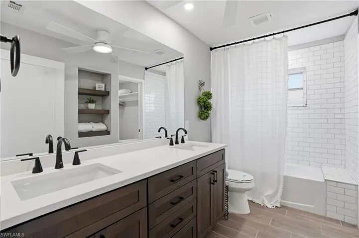 Bathroom featuring double vanity, ceiling fan, wood tiled floors, shower / bathtub combination with curtain, and recessed lighting - Virtually Edited Image