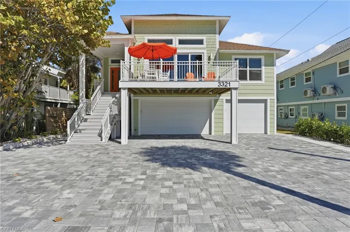 Raised beach house featuring an attached garage, decorative driveway, and a balcony - Virtually Edited Image