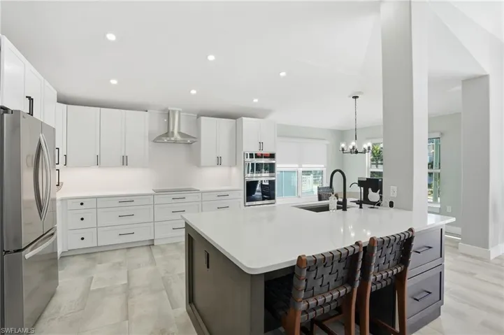 Kitchen with stainless steel appliances, a kitchen island with sink, suspended lighting, dual tone cabinetry, and light stone counters - Virtually Edited Image