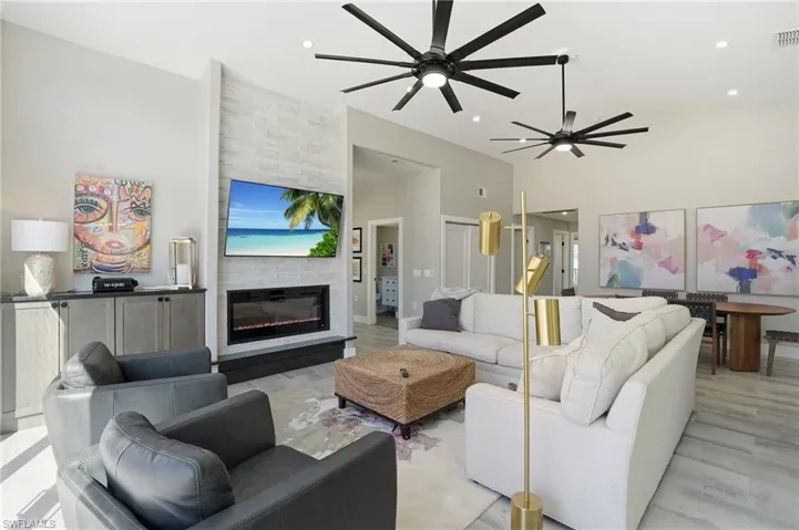 Living room featuring a large fireplace, ceiling fan, vaulted ceiling, and wood finished floors - Virtually Edited Image