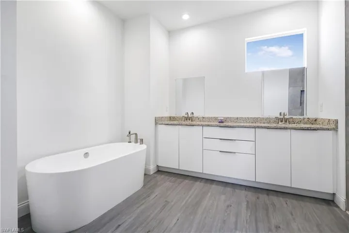 Bathroom featuring double vanity, wood finished floors, a soaking tub, and a sink