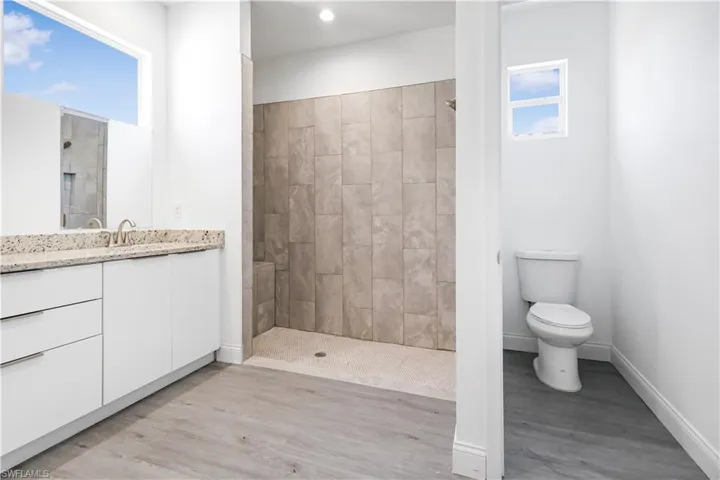 Bathroom with baseboards, toilet, wood finished floors, vanity, and tiled shower