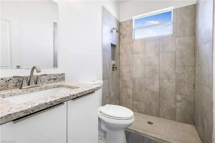 Bathroom featuring toilet, a tile shower, and vanity