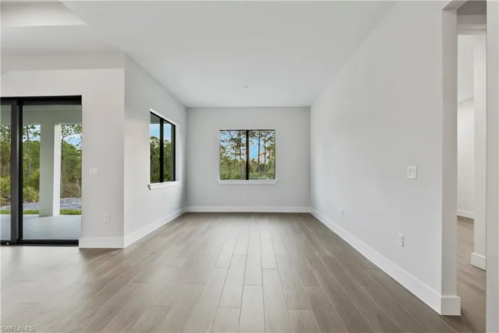 Spacious interior room with wood-finish flooring, multiple windows, and a large sliding glass door opening to a covered patio