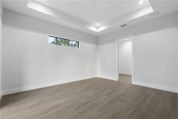 Spacious room featuring wood-finish flooring, a tray ceiling with recessed lighting, and a horizontal window