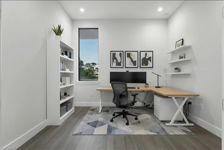 Dedicated workspace featuring wood-finish flooring, a tall built-in bookshelf, a large window, and recessed lighting