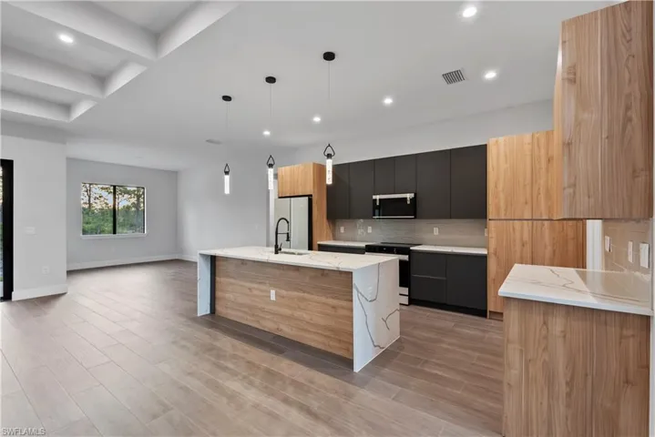 Modern kitchen featuring a waterfall island with a quartz countertop, wood-finish cabinetry, matte black hardware, and pendant lighting
