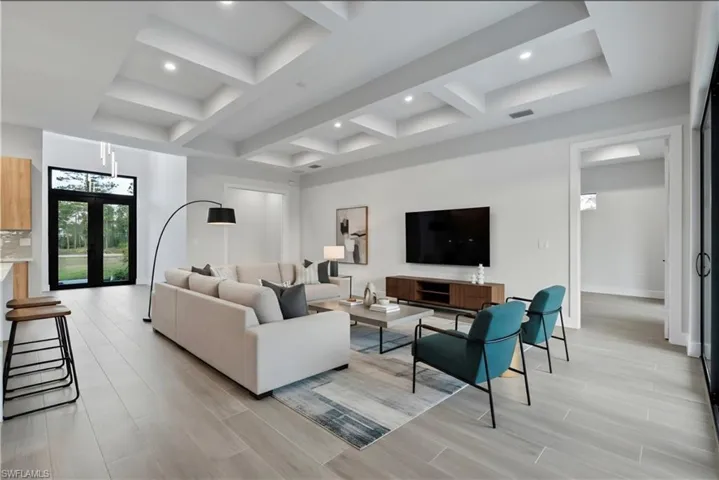 Open-concept living space featuring coffered ceilings with recessed lighting, light wood-finish flooring, and white walls