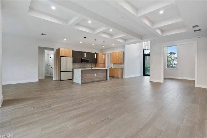Open-concept living area with wood-look tile flooring, tray ceilings with recessed lighting, and a contemporary kitchen featuring a large island with waterfall countertop, two-tone cabinetry, and modern pendant lighting