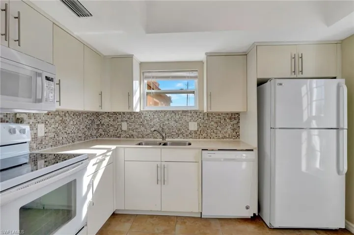 Kitchen with white appliances, cream cabinetry, backsplash, and light tile patterned floors