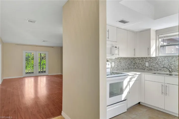 Kitchen with white appliances, backsplash, light countertops, french doors, and light wood-type flooring