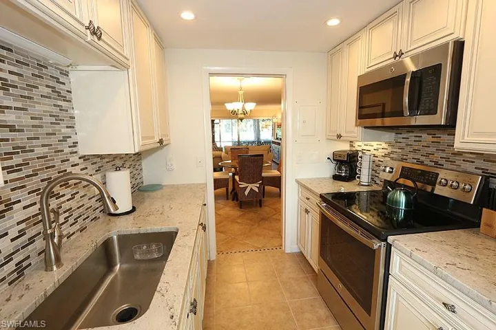 Kitchen with backsplash, appliances with stainless steel finishes, sink, and light tile flooring