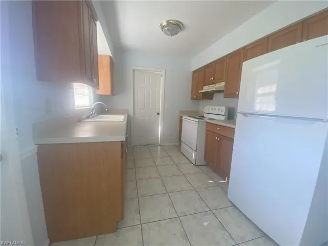 Kitchen featuring white appliances, sink, and light tile patterned flooring