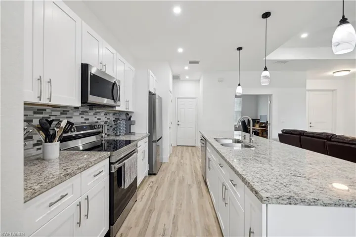 Kitchen featuring appliances with stainless steel finishes, hanging light fixtures, sink, and white cabinets