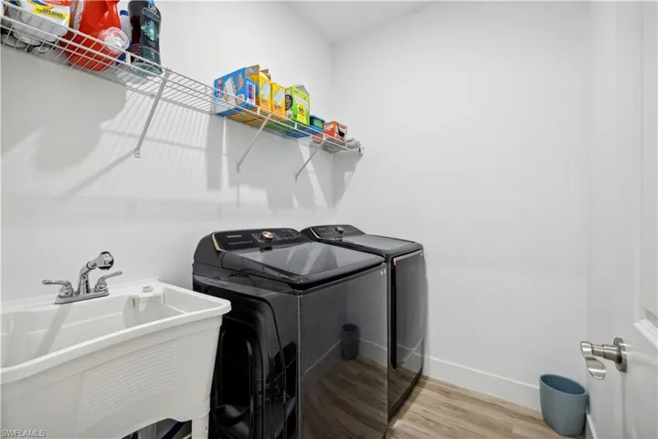 Clothes washing area with wood-type flooring, sink, and washing machine and dryer