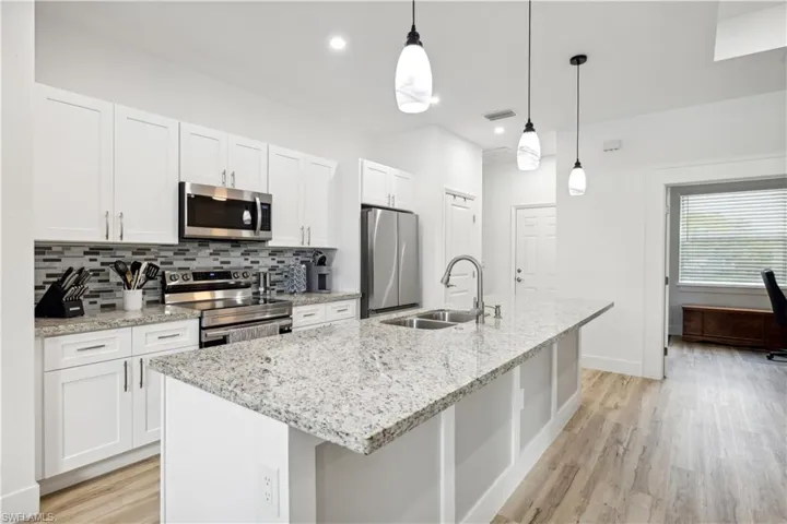 Kitchen with appliances with stainless steel finishes, hanging light fixtures, an island with sink, white cabinets, and sink