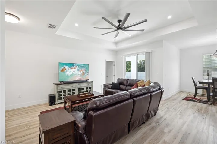 Living room featuring light wood-type flooring, a tray ceiling, and ceiling fan