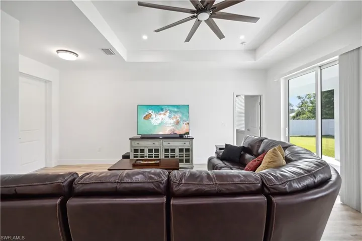 Living room with ceiling fan, a tray ceiling, and light hardwood / wood-style floors