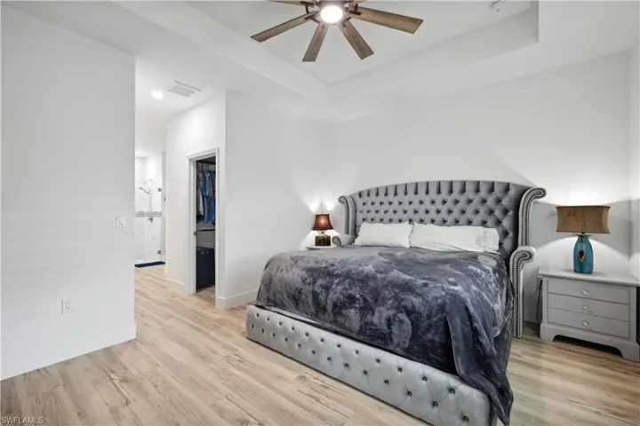 Bedroom with light hardwood / wood-style floors, ceiling fan, a tray ceiling, and ensuite bath