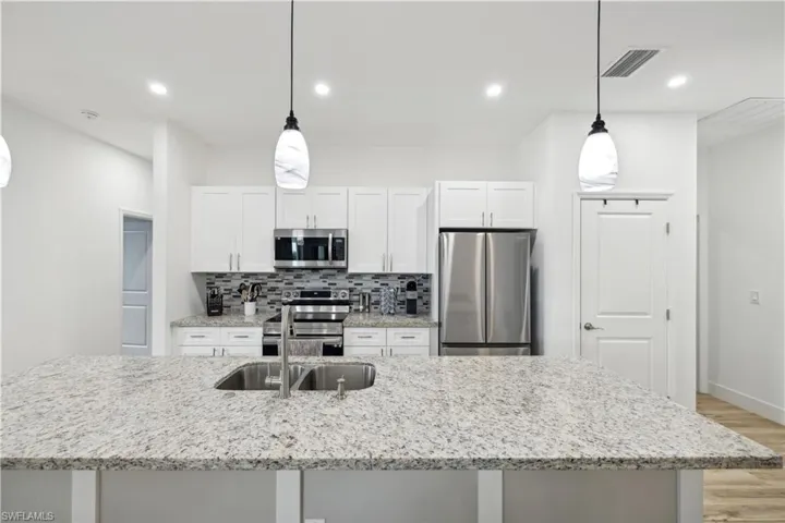 Kitchen with a kitchen island with sink, white cabinetry, stainless steel appliances, and decorative light fixtures
