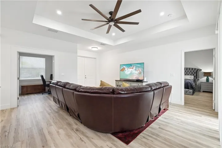 Living room featuring ceiling fan, a tray ceiling, and light hardwood / wood-style floors