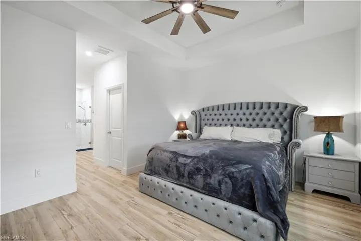 Bedroom with ceiling fan, light wood-type flooring, and a tray ceiling