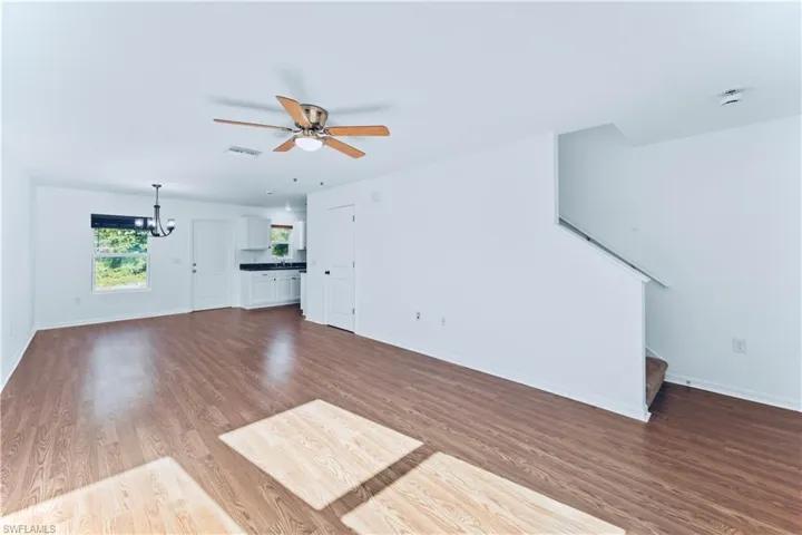 Unfurnished living room featuring ceiling fan with notable chandelier, visible vents, stairs, baseboards, and dark wood-style floors