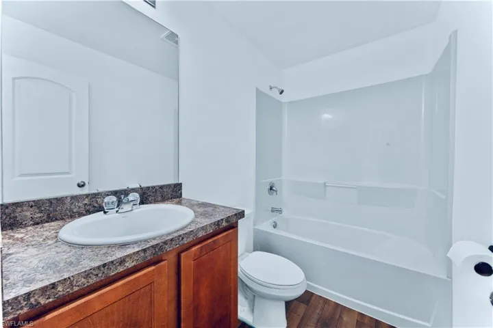 Bathroom featuring vanity, toilet, visible vents, tub / shower combination, and wood finished floors