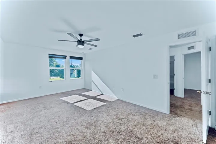 Carpeted empty room with visible vents, ceiling fan, and baseboards