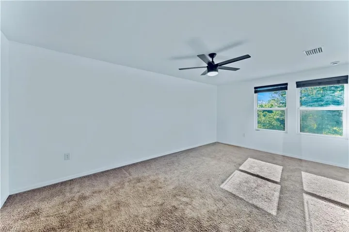 Spare room featuring carpet flooring, visible vents, baseboards, and ceiling fan
