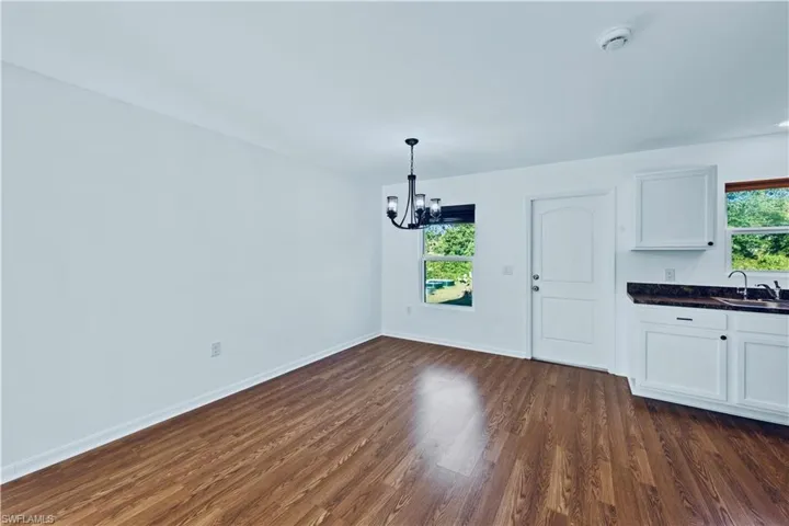 Unfurnished dining area featuring a sink, dark wood-type flooring, baseboards, and an inviting chandelier