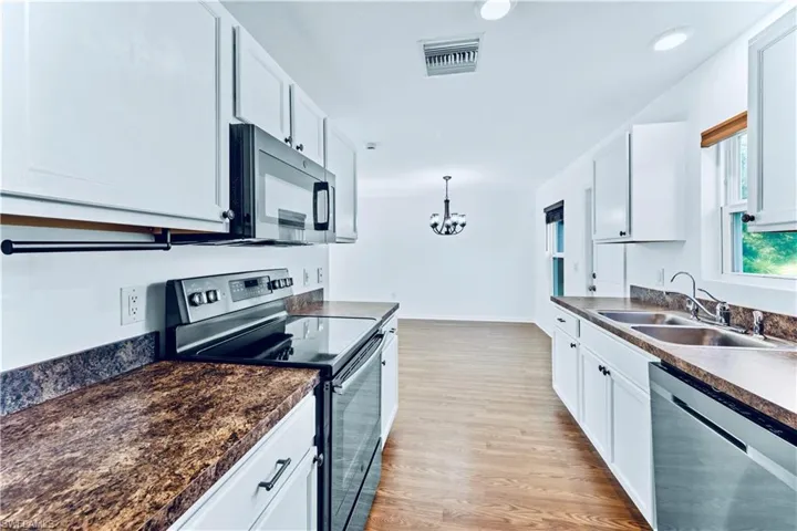 Kitchen with black microwave, stainless steel electric range oven, dark countertops, dishwashing machine, and a sink