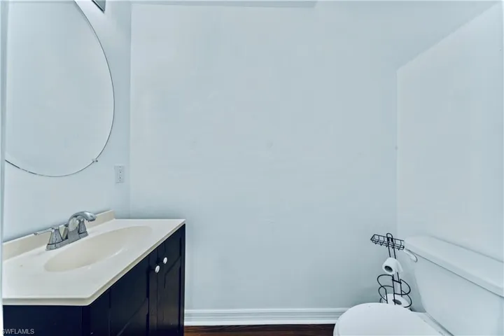 Half bath featuring toilet, vanity, wood finished floors, and baseboards