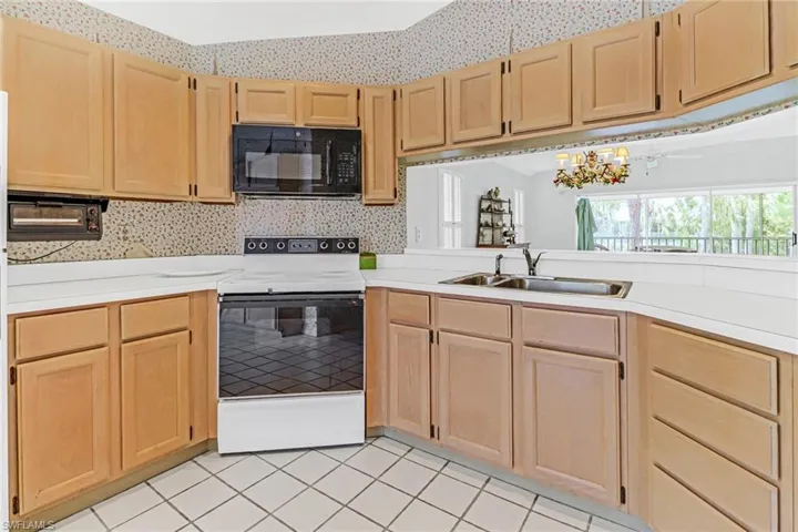 Kitchen with light brown cabinets, white range with electric cooktop, sink, and light tile flooring