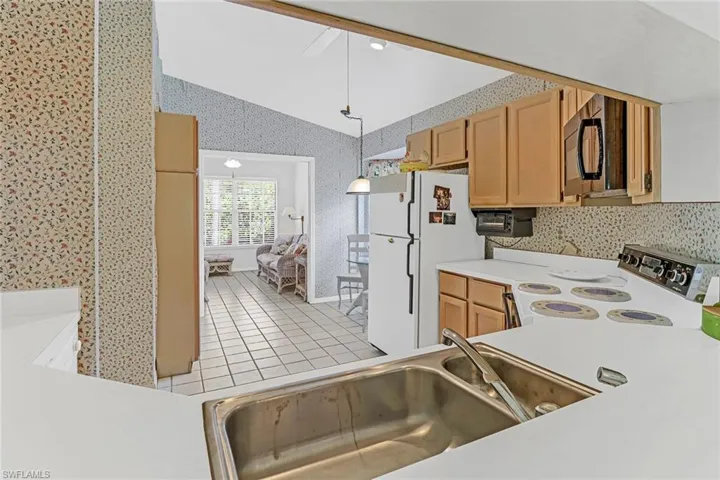 Kitchen featuring white refrigerator, lofted ceiling, range, sink, and pendant lighting