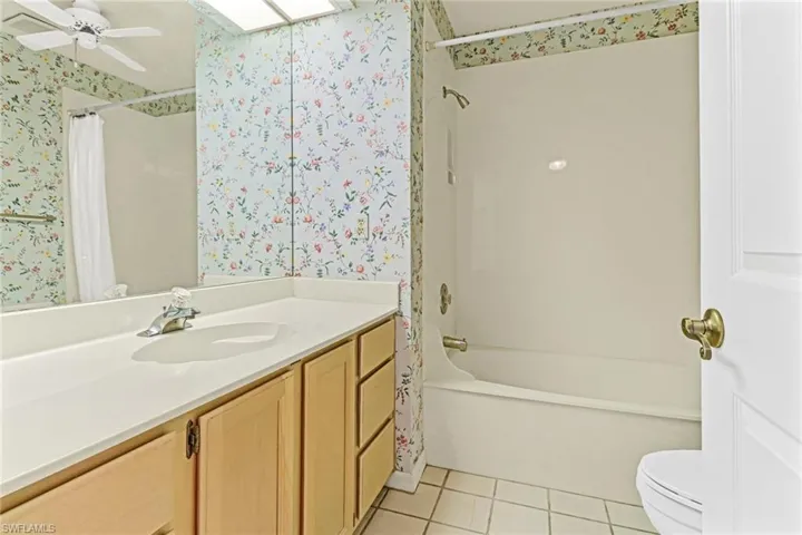 Full bathroom with shower / bathtub combination with curtain, tile flooring, ceiling fan, vanity, and toilet
