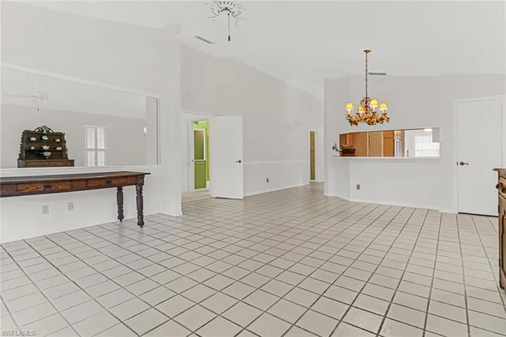 Unfurnished living room with high vaulted ceiling, light tile flooring, and ceiling fan with notable chandelier