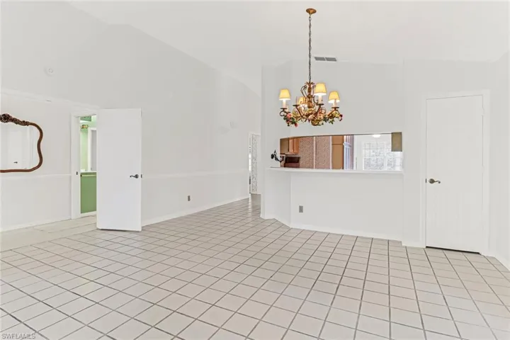 Spare room with high vaulted ceiling, light tile flooring, and an inviting chandelier