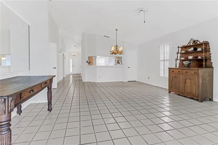 Unfurnished living room featuring an inviting chandelier, lofted ceiling, and light tile floors