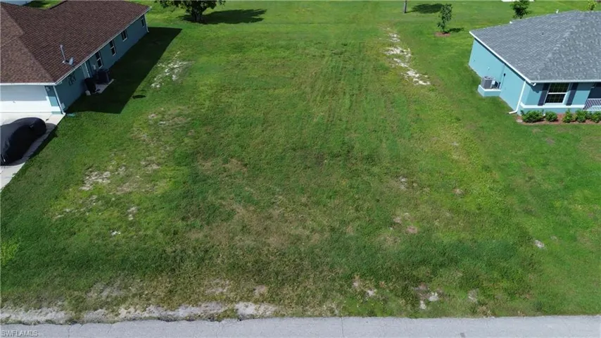 Expansive undeveloped lot with grass coverage, positioned between two residential structures